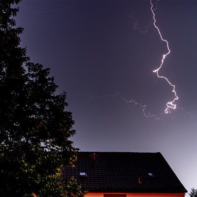 lightning in night sky above house and tree